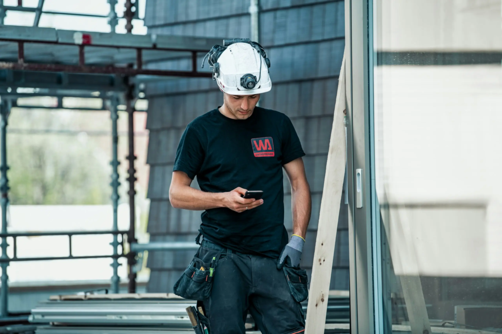 Medarbejder på byggeplads registrerer sikkerhedsdata på sin telefon – digital arbejdsmiljøledelse i praksis